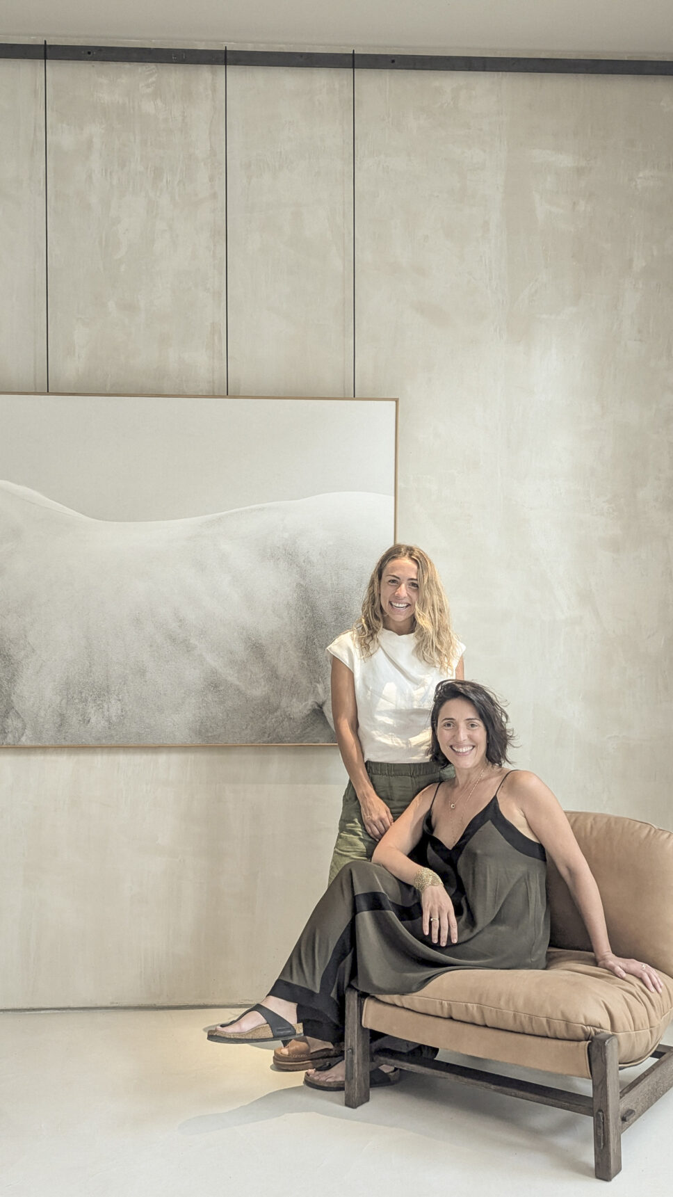 White horse photograph from BERNI by Emilia Brandão Carneiro, displayed above two armchairs at Lorna de Santos’s studio in Madrid with Emilia and Lorna posing in front of it.